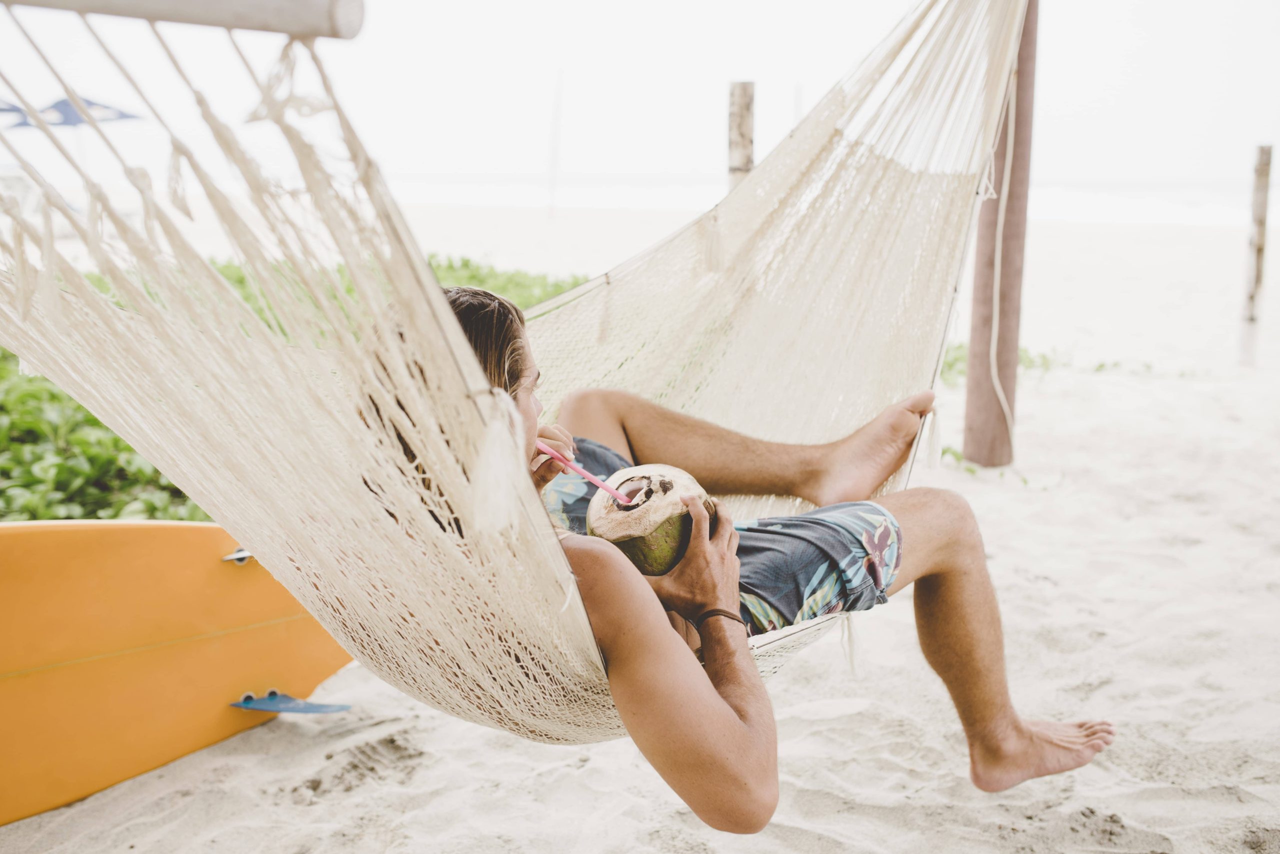 Man enjoying coconut water in hammock on beach